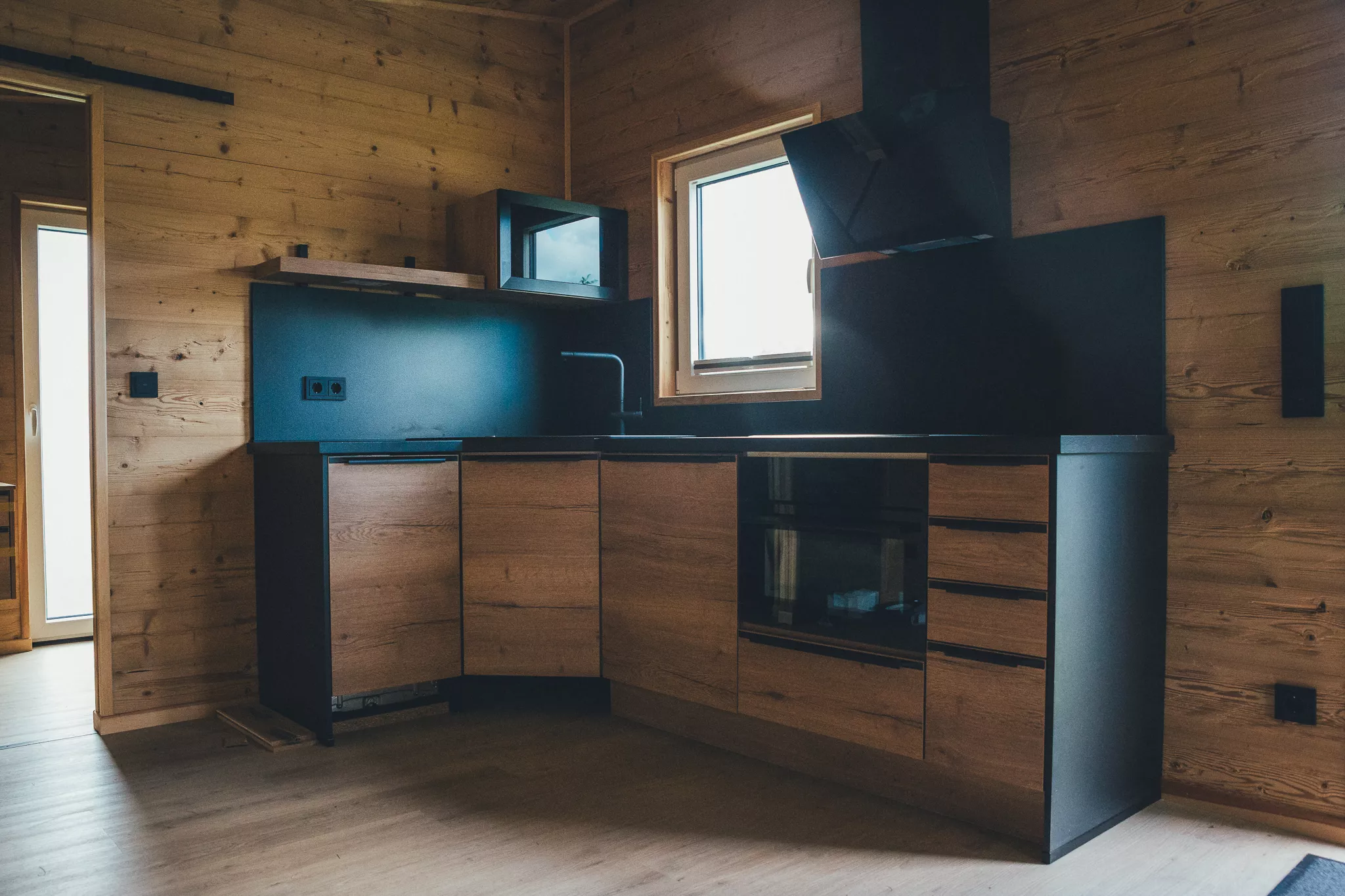 Kompakte Küche im Tiny House mit Holzfronten, Herd, Spüle und Fenster